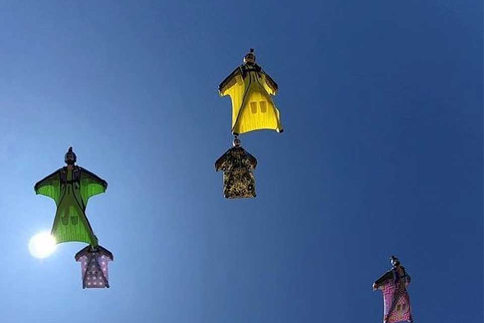 A group of people flying wingsuits with the bright blue sky behind them.
